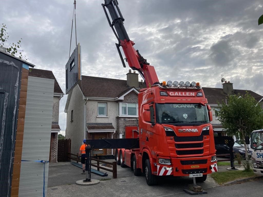 Crane lifting prefabricated panel for home extension by Shanette over house roof